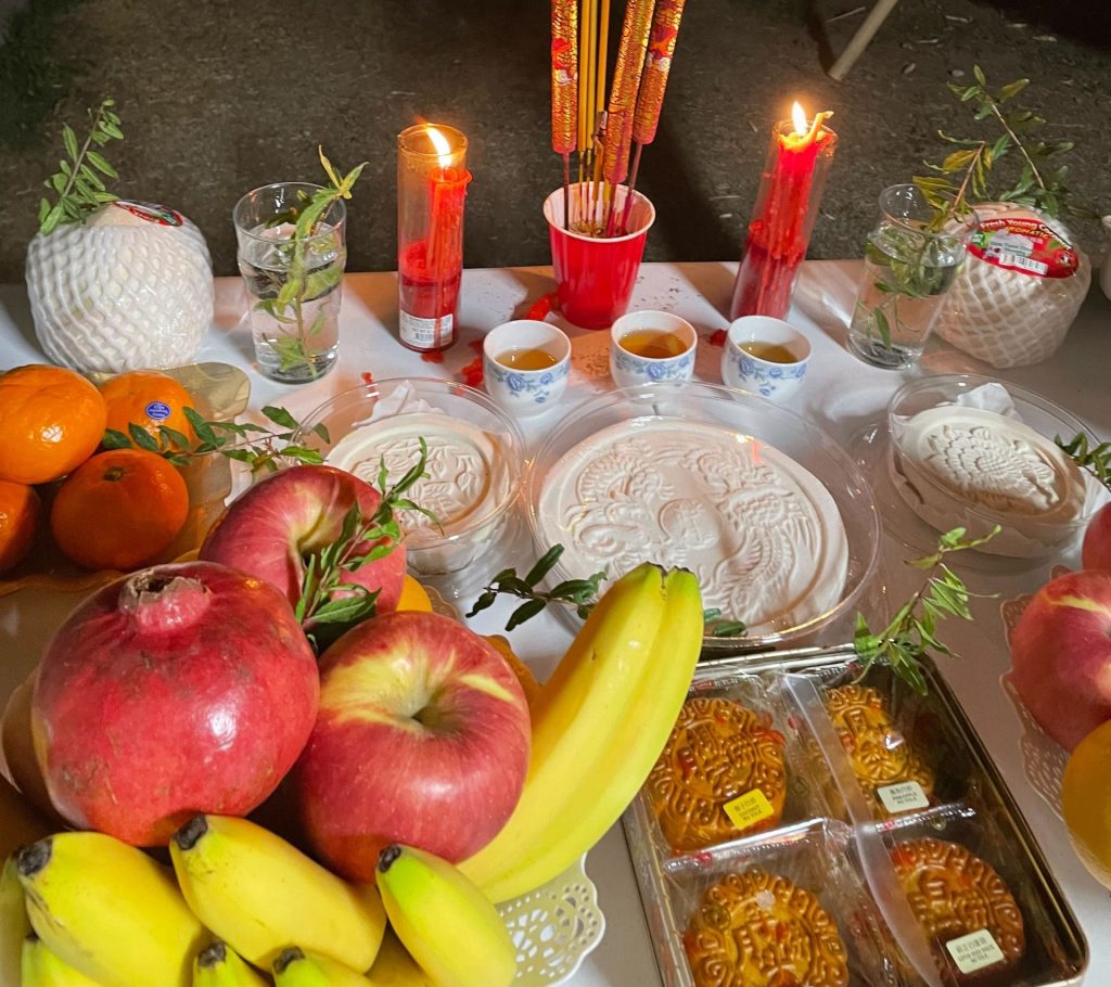 Picture of a table filled with fruits, mooncake, flowers, and candles.
